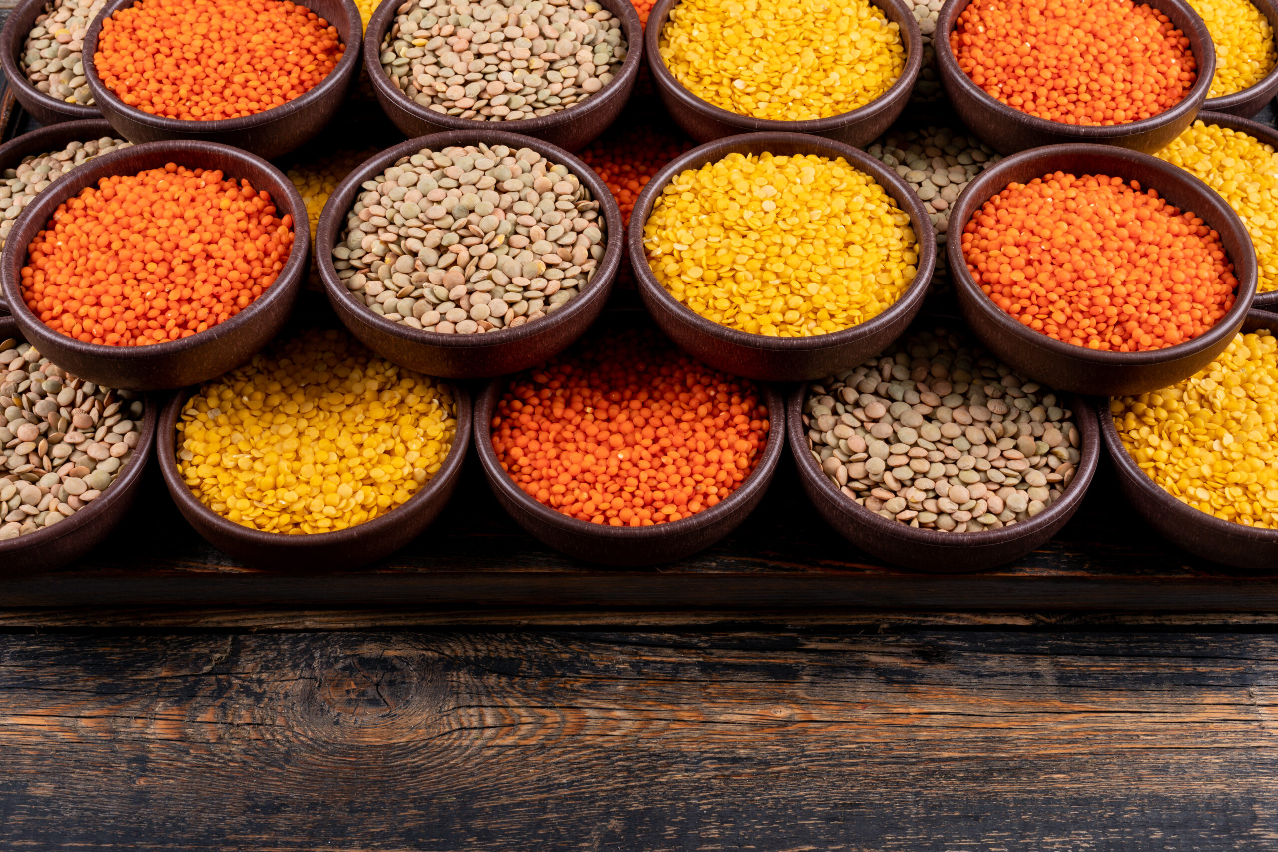 some of yellow, green and red lentils in a brown bowls on dark wooden background, high angle view. free space for your text